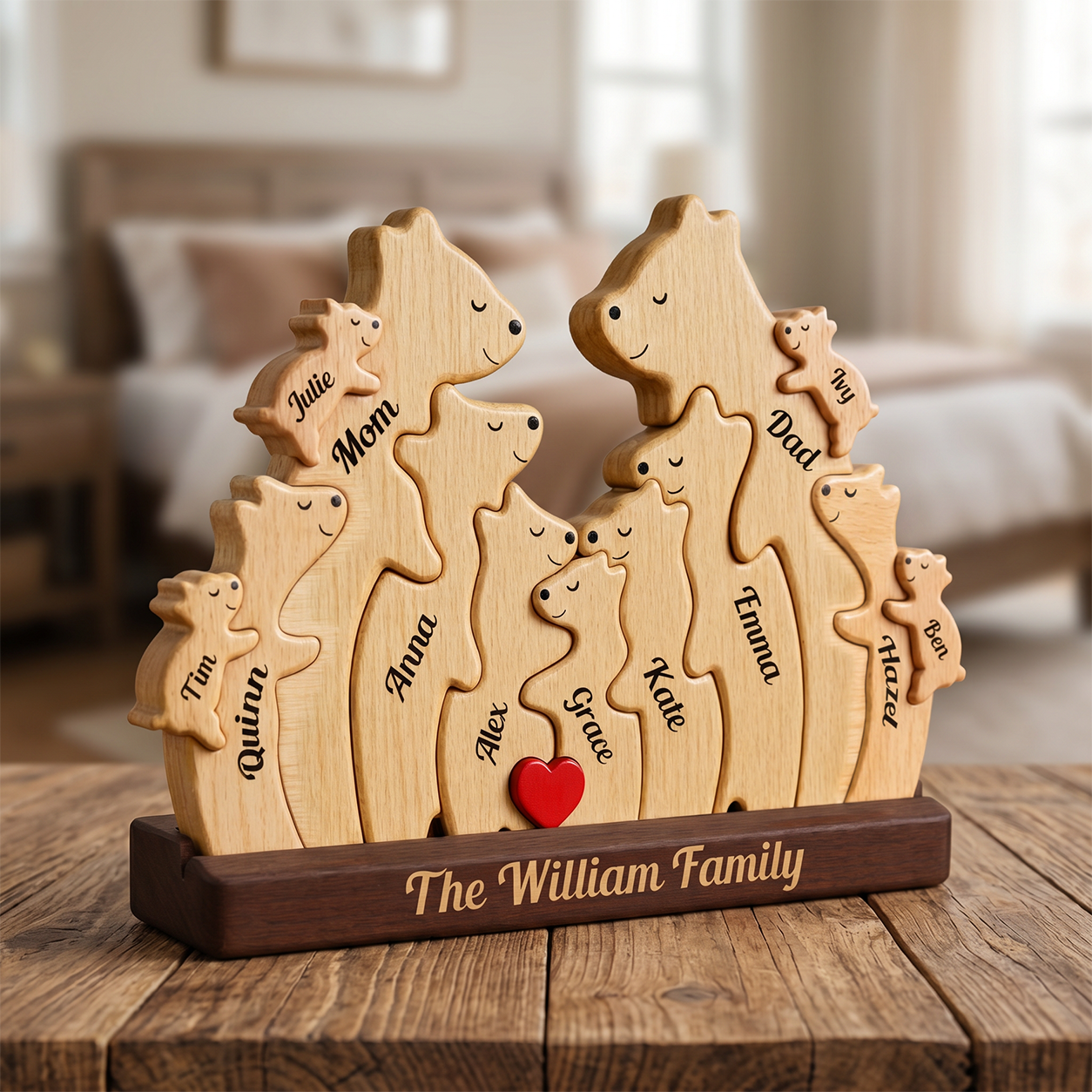 Personalized wooden family plaque shaped, engraved with names and a small red heart, displayed on a wooden table in a softly blurred bedroom setting.