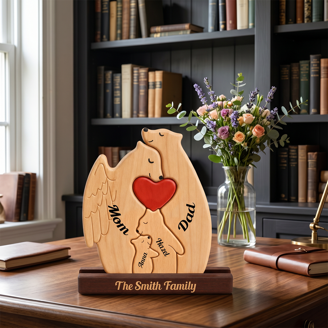 Personalized wooden Mom and Dad bear figurines with a red heart, displayed on a wooden stand on a desk in a study setting with a vase of flowers and bookshelves in the background.