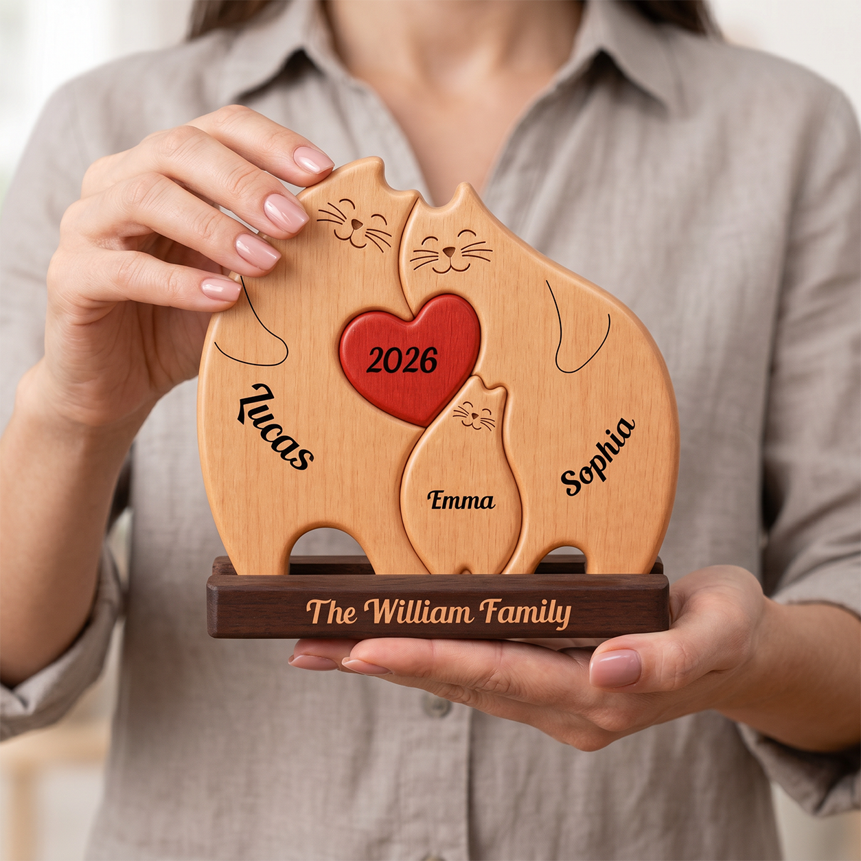A person in a light gray shirt holds a personalized wooden keepsake plaque shaped like three cats. 