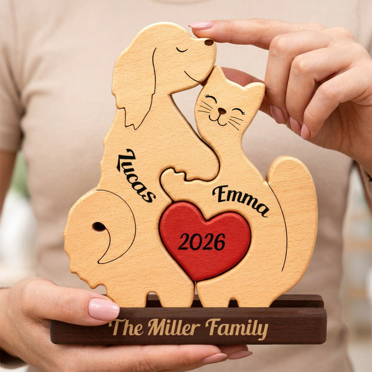 Personalized wooden pet couple plaque shaped like a dog and cat with a red heart and engraved names, held by hands against a soft beige background.