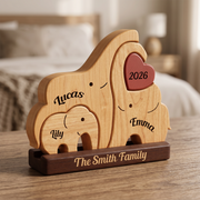 Personalized wooden family elephant keepsake box on a wooden table with a blurred bedroom background. The set includes three interlocking elephant-shaped compartments in light natural wood, a dark brown base printed names