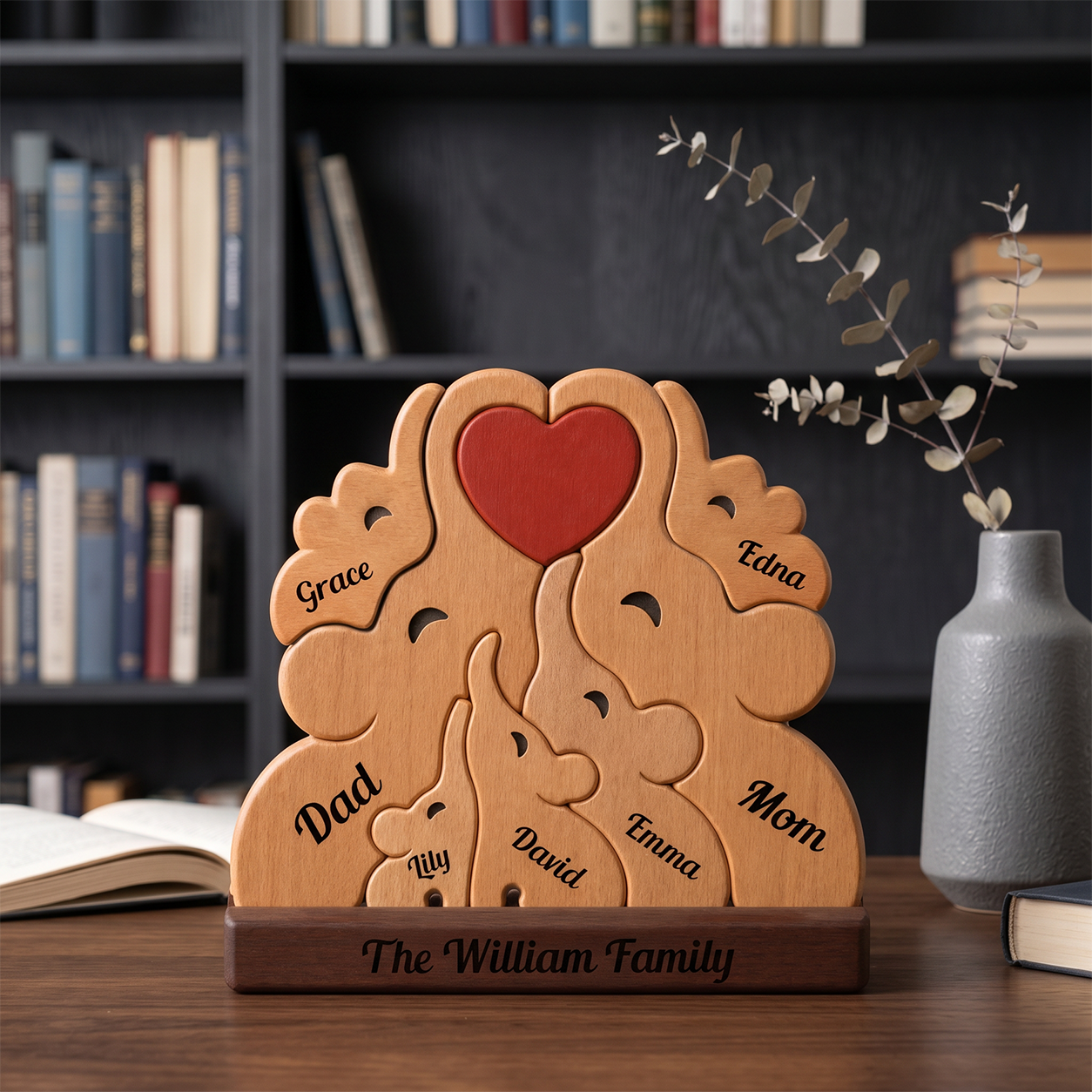 Wooden family decoration with engraved names on a wooden base, placed on a desk with books and a vase in the background.