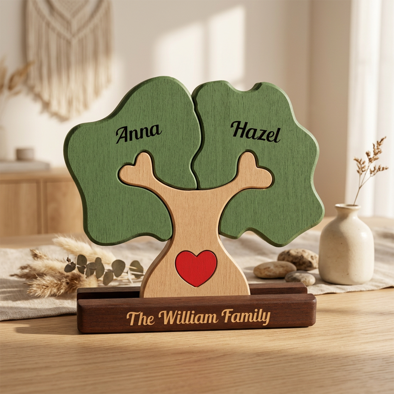Personalized wooden family tree plaque on a tabletop, with green leaves labeled Anna and Hazel, a light wood trunk with a red heart, and a dark wood base engraved with The Family Names.