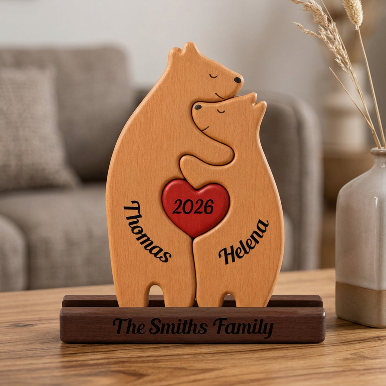 Wooden bear sculpture with '2026' heart and engraved names on a wooden stand, placed on a table.