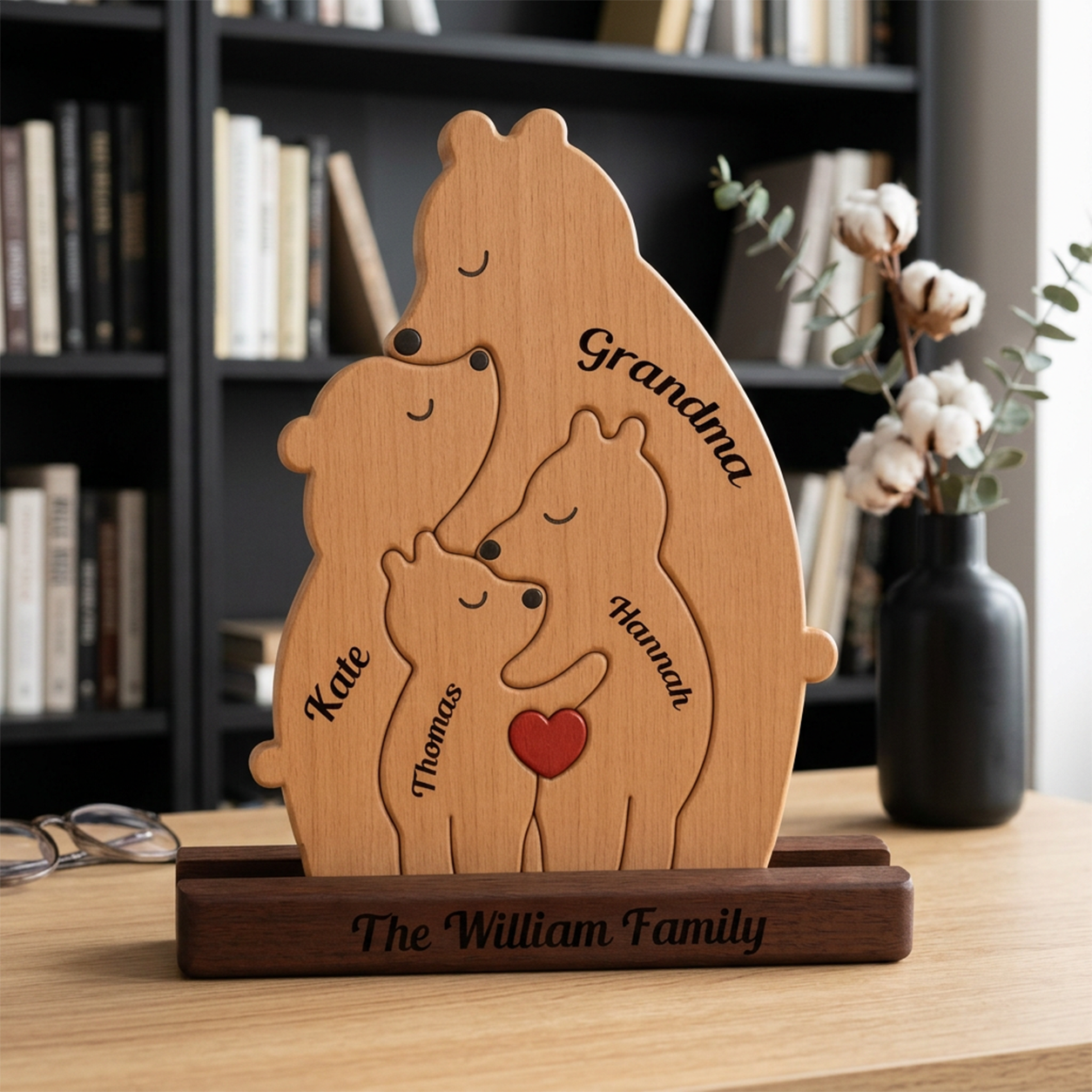 Wooden family sculpture with engraved names on a wooden base, placed on a table with a bookshelf in the background.