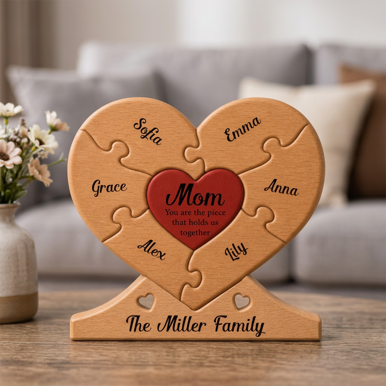 Wooden heart-shaped puzzle with engraved names and 'Mom' in a red heart, placed on a wooden surface with a blurred background.