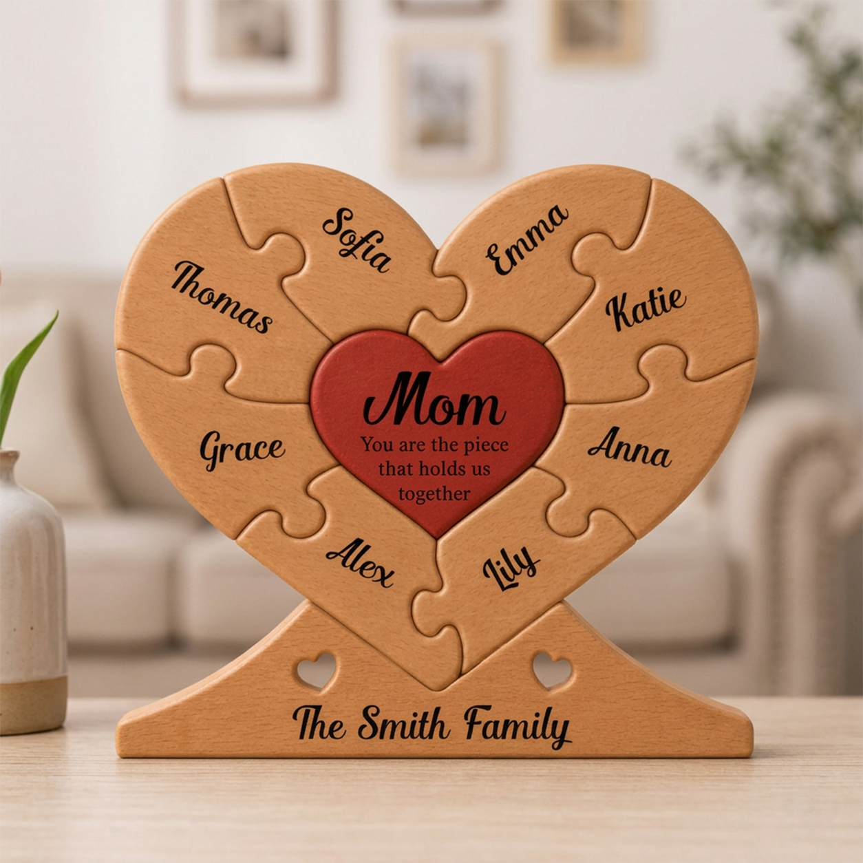 Heart-shaped wooden puzzle with engraved names and 'Mom' in a red heart, placed on a surface.