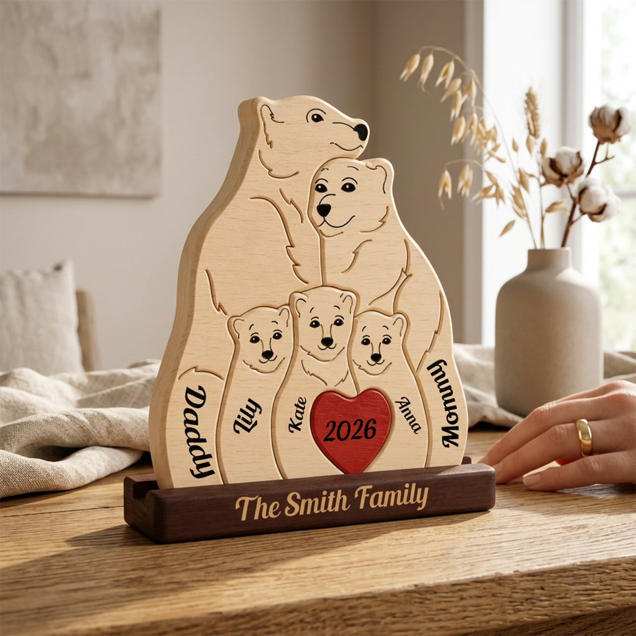 Personalized wooden family tree plaque with engraved polar bear illustrations, a red heart reading 2026, and a dark base engraved 'The Family.' A hand with a gold ring is touching the right side of the plaque.