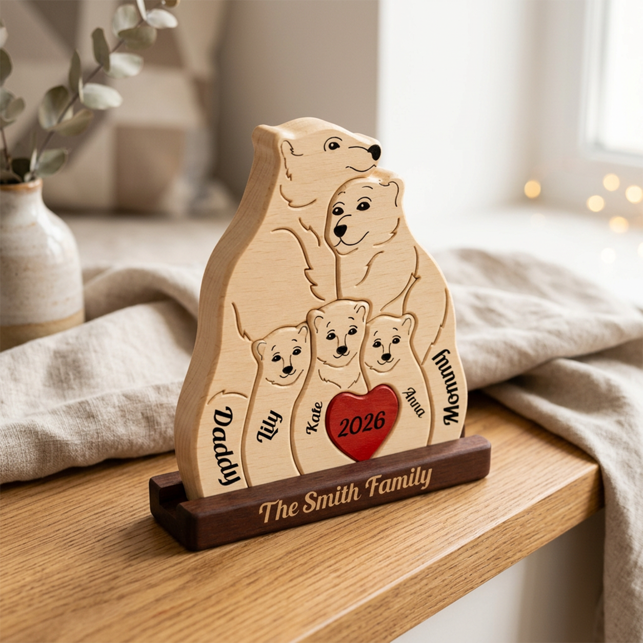Personalized wooden family bear plaque with engraved names and a red heart reading 2026, displayed on a wooden stand in a softly lit indoor setting.